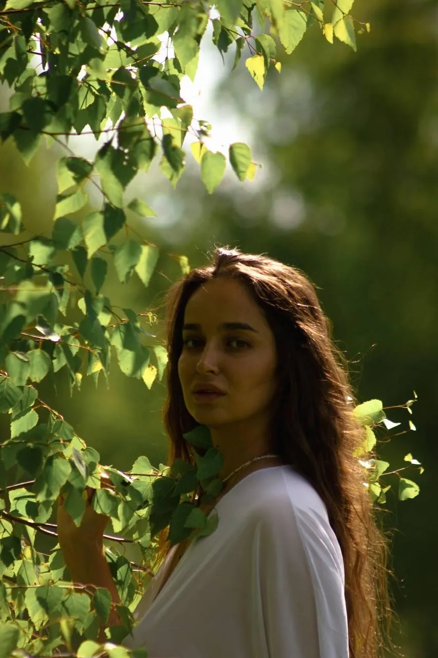 Woman in a White Blouse Walking Through a Sunlit Forest
