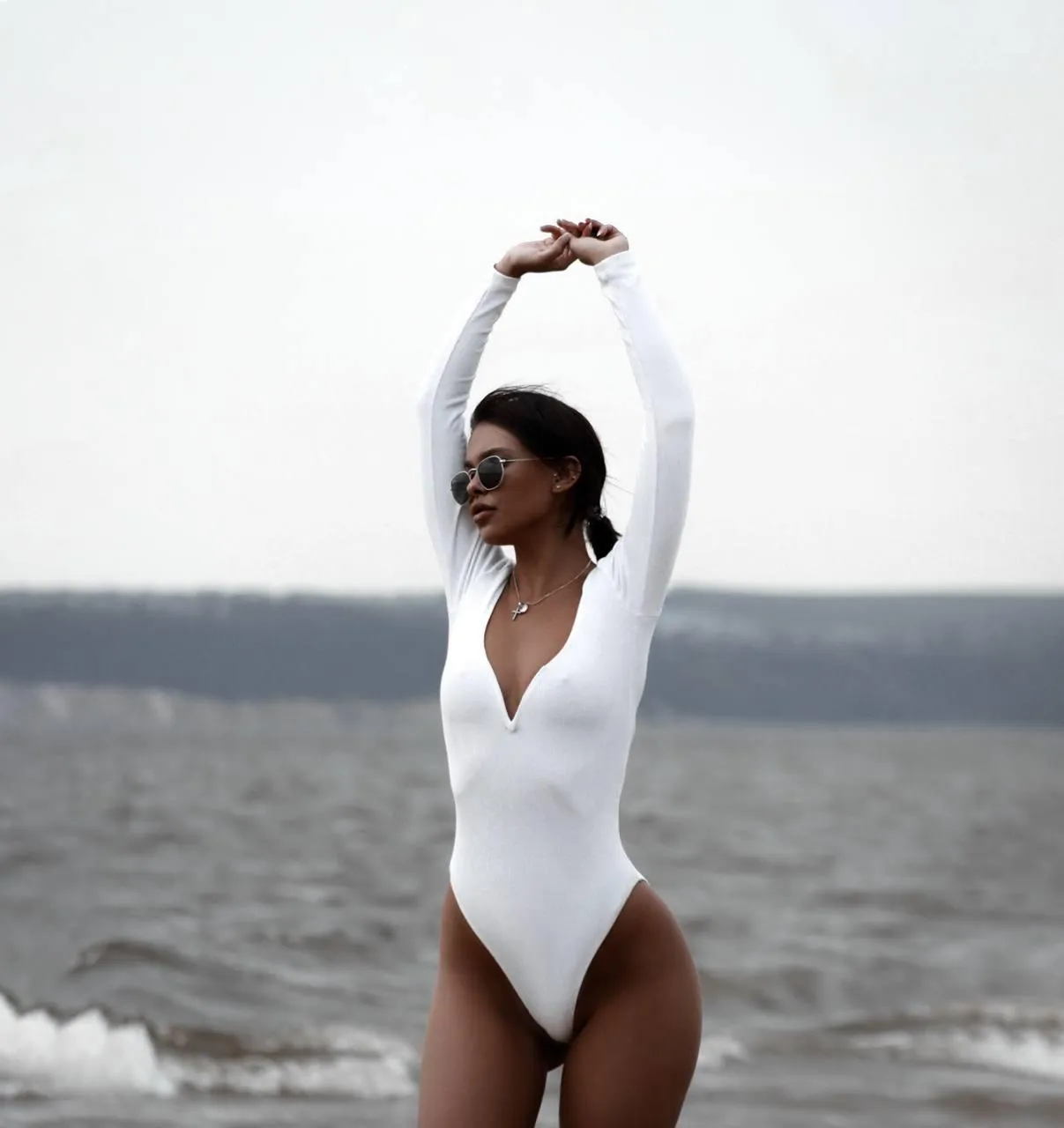 Woman in a white bodysuit posing gracefully on a sandy beach