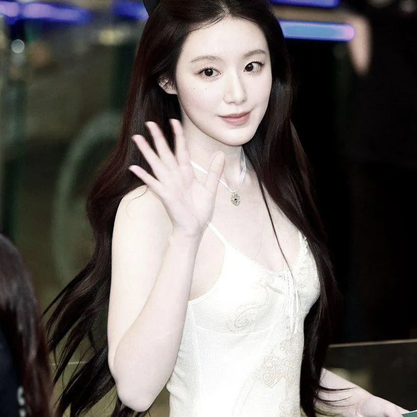 Woman in a white dress waving and smiling at a public event