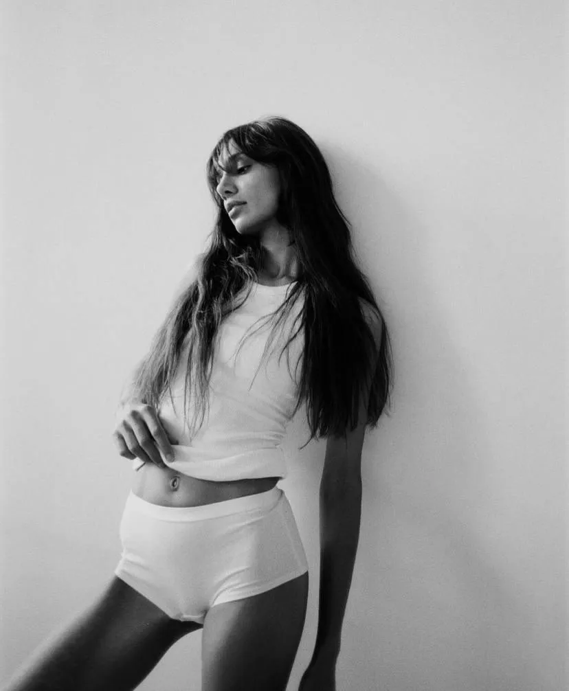 Woman in a white outfit standing near a wall grayscale image