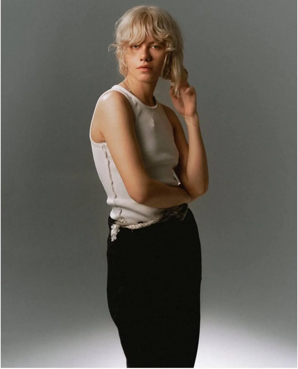 Woman in a white tank top and black skirt posing confidently