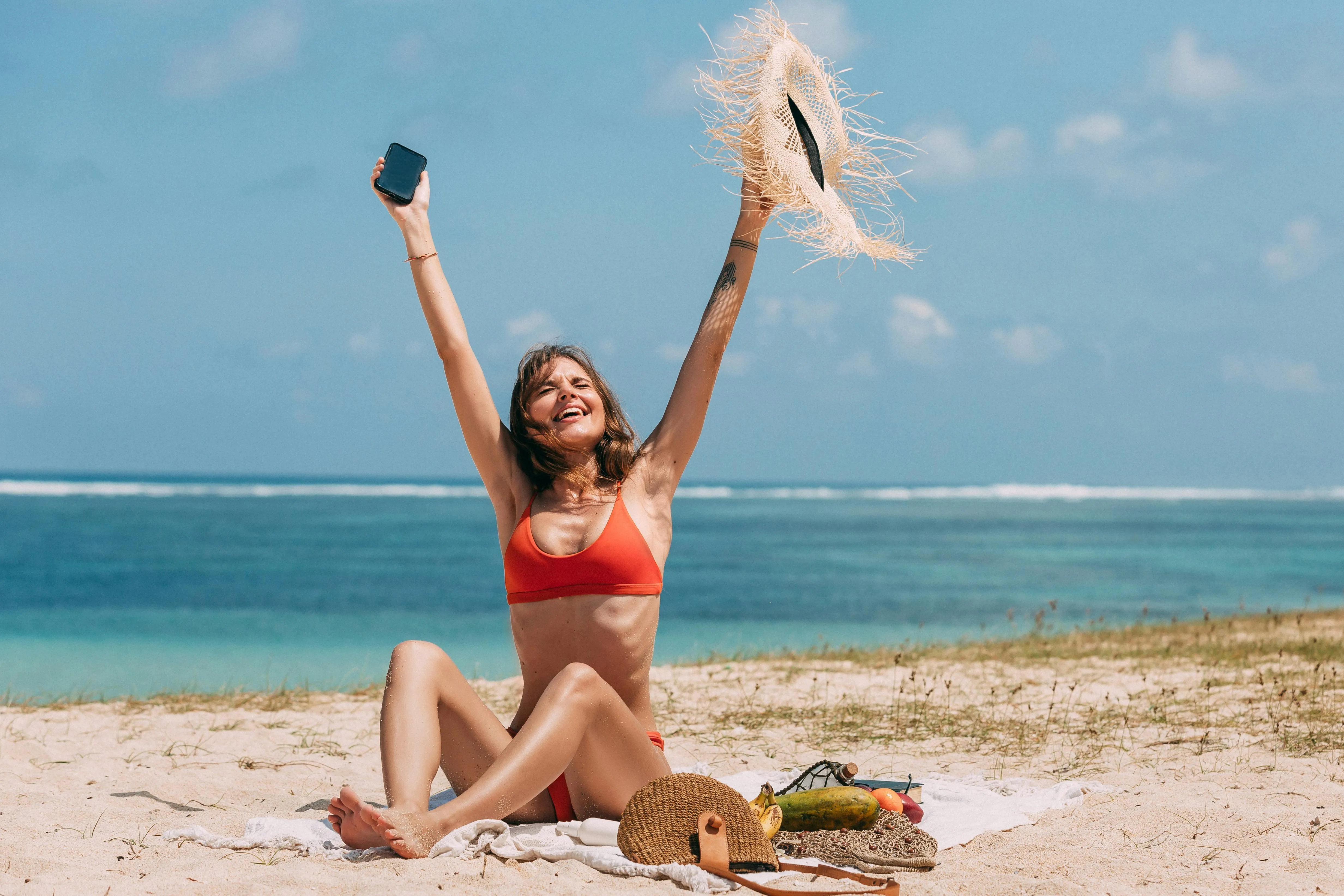 Woman in an Orange Bikini Sitting And Waving on the Beach