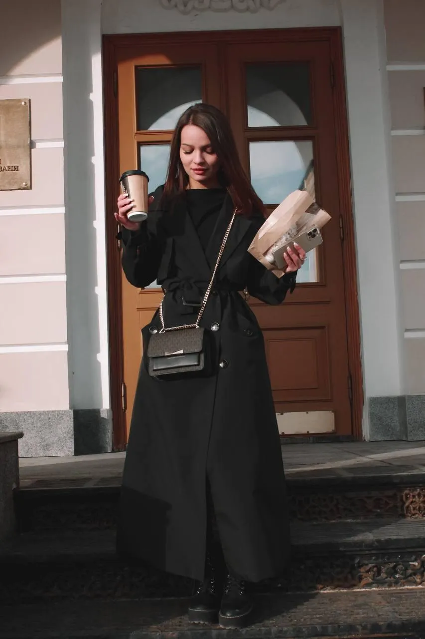 Woman in black coat holding a bag walking near the building