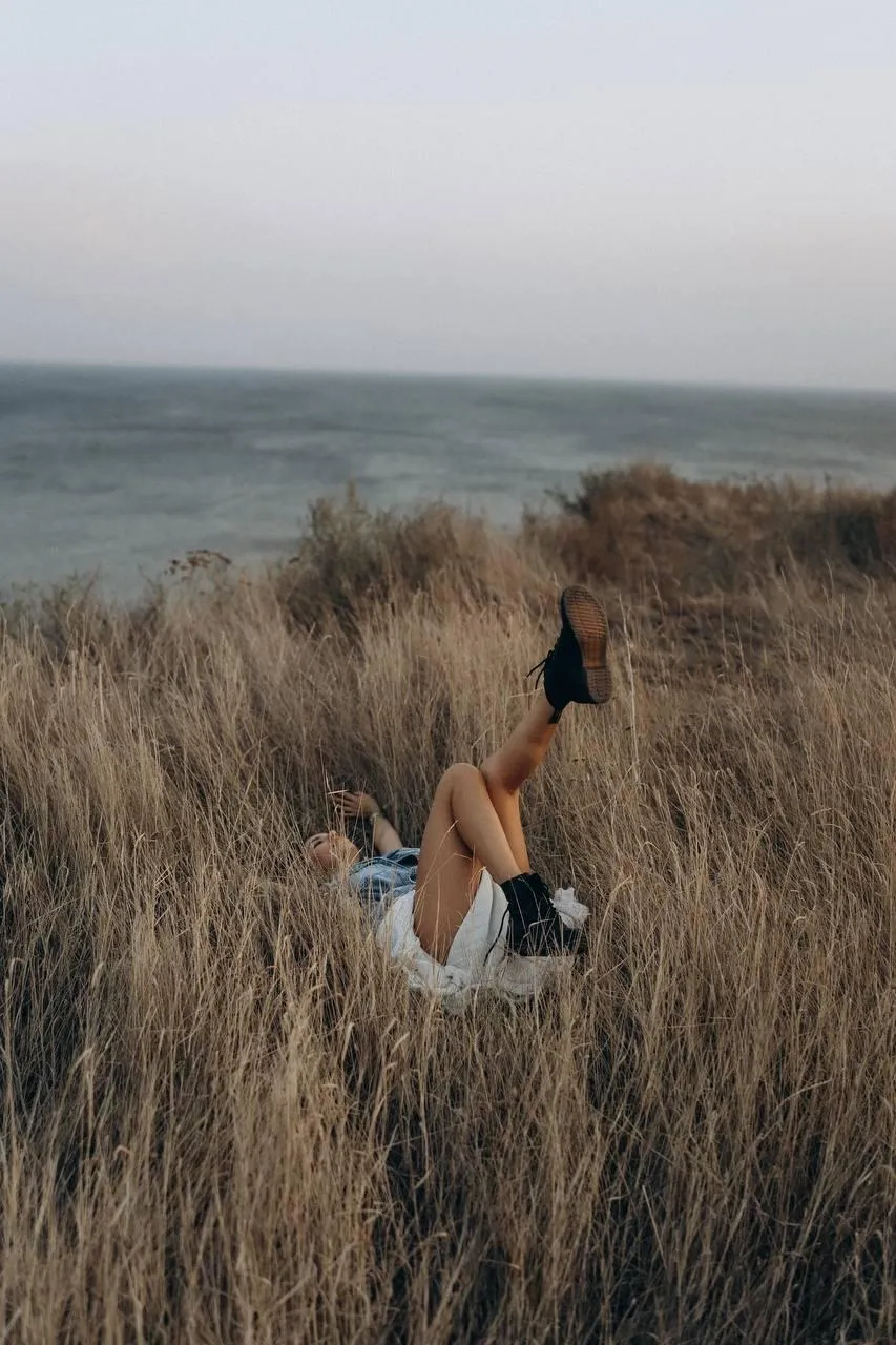 Woman in Black Outfit Sitting in Tall Dry Grass Near the Sea