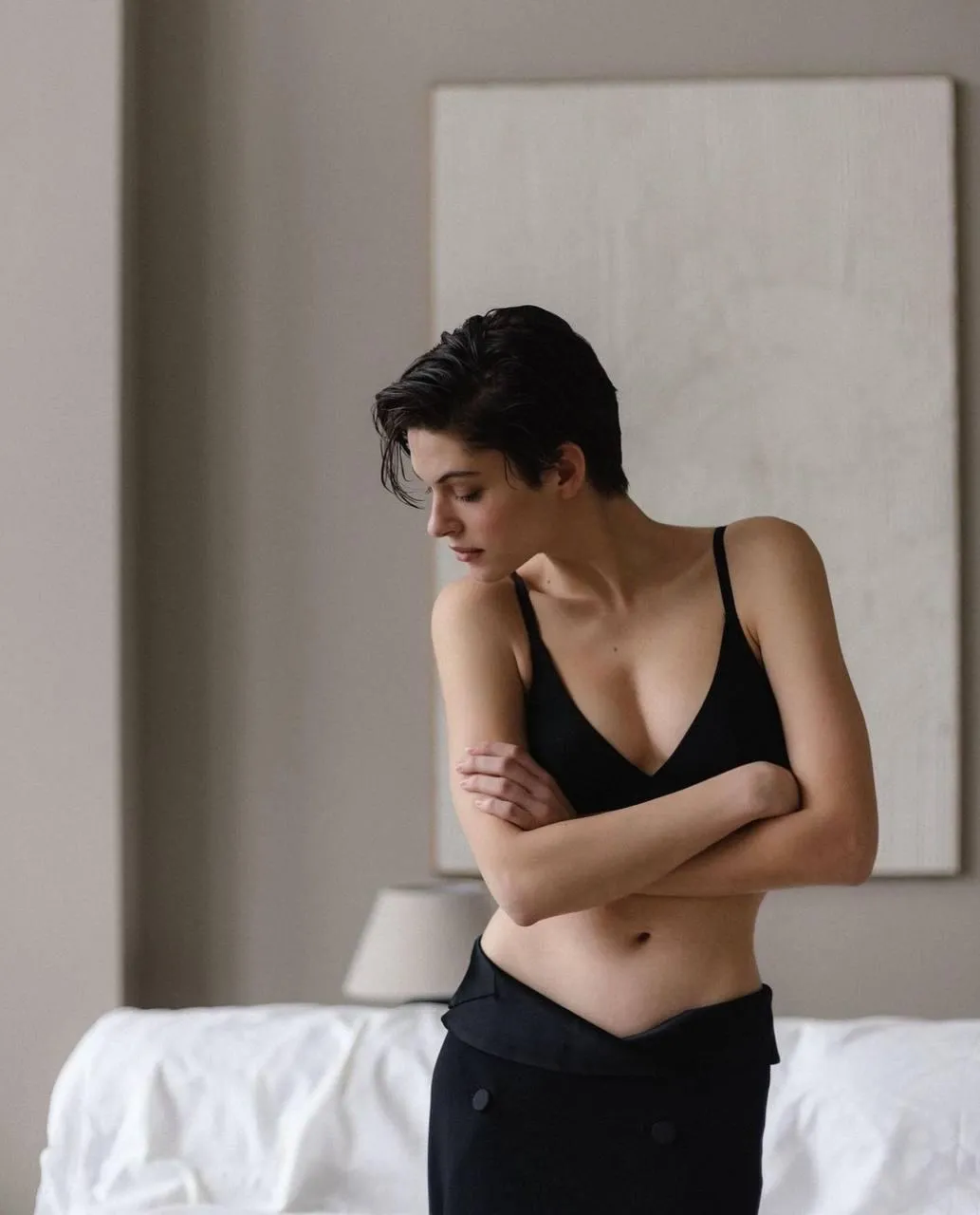 Woman in black pants posing in soft light by the bed frame
