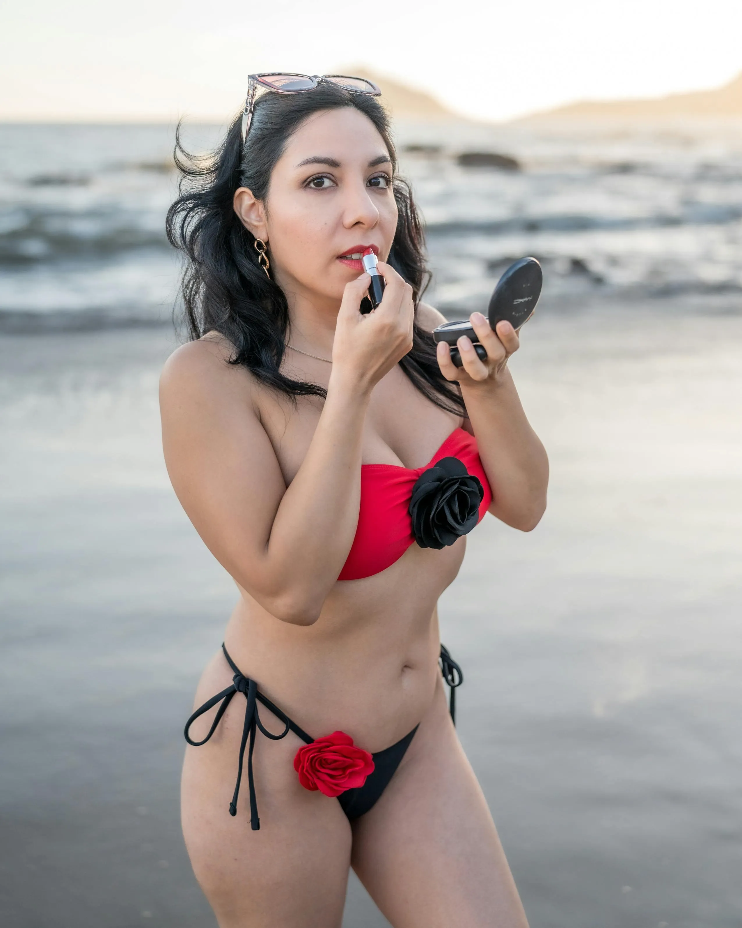 Woman in Floral Bikini Applying Lipstick on Beach at Sunset