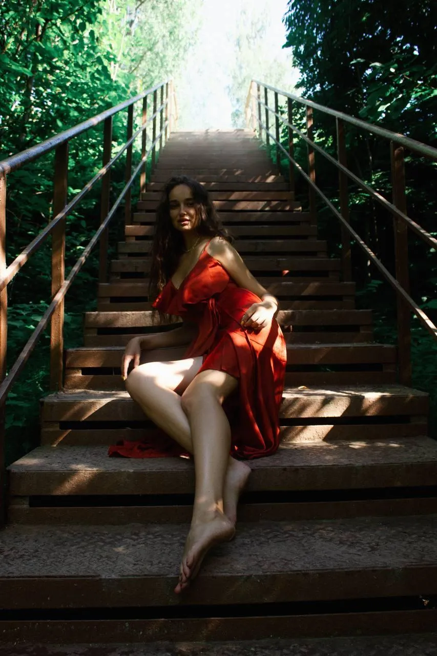 Woman in Red Dress Sitting on Stairs Under Natural Sunlight
