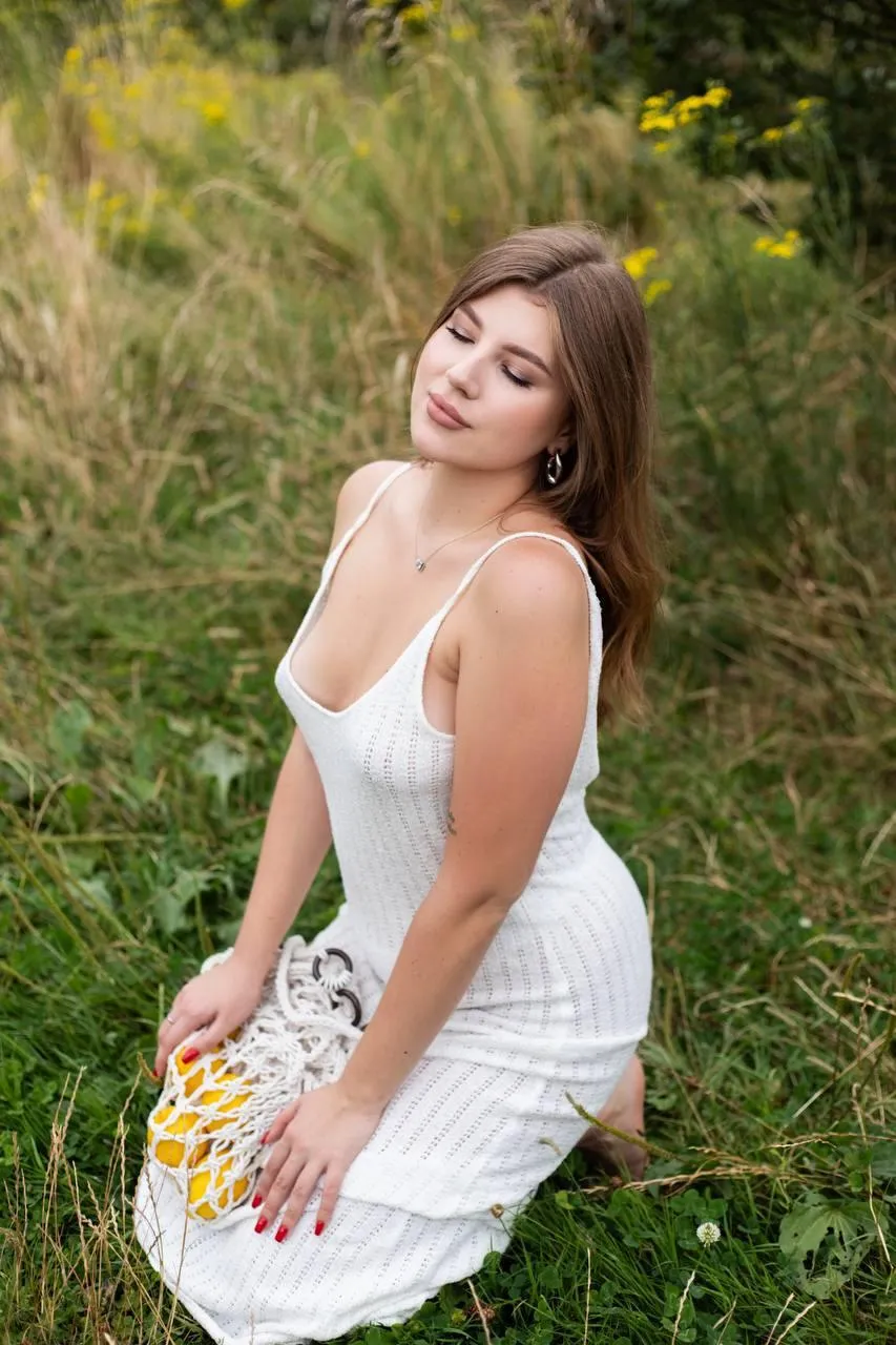 Woman in White Dress Sitting in Grassy Field Smiling Gently