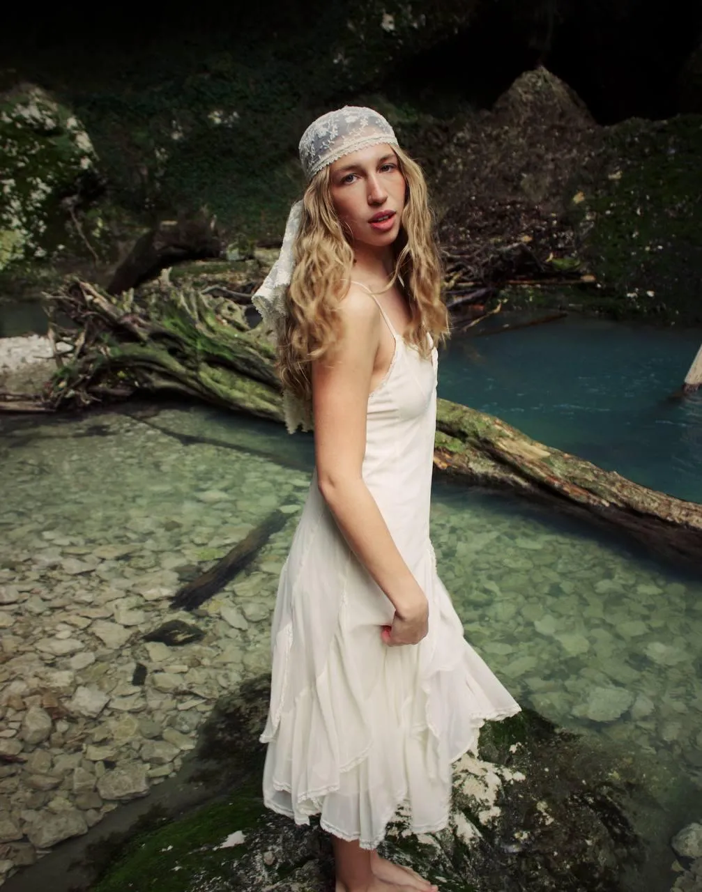 Woman in White Dress Standing by River with Nature Backdrop