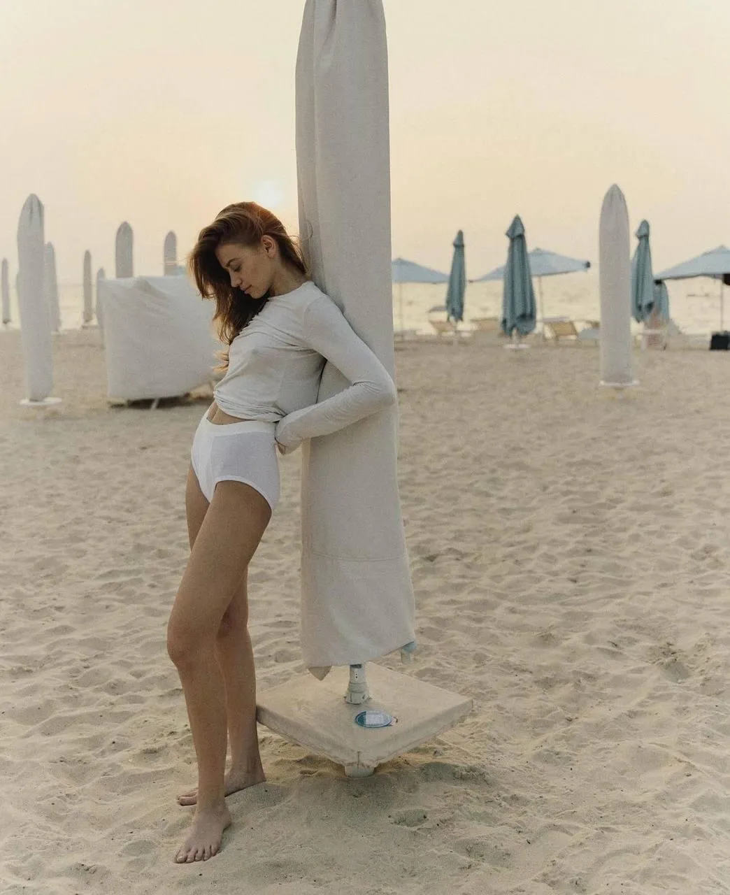 Woman in White Dress Standing on Sandy Beach Near Surfboards