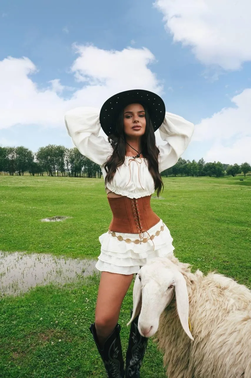 Woman in White Outfit And Black Hat Posing in Green Field