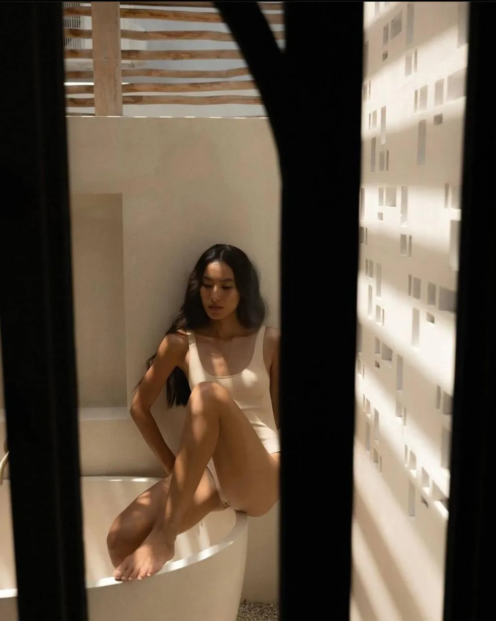 Woman in white outfit standing in a shadowy hallway indoors