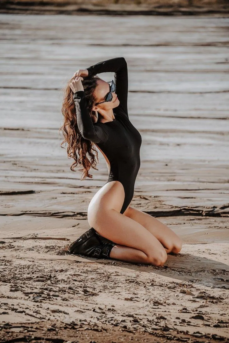 Woman Kneeling on a Sandy Beach in an Elegant Black Outfit