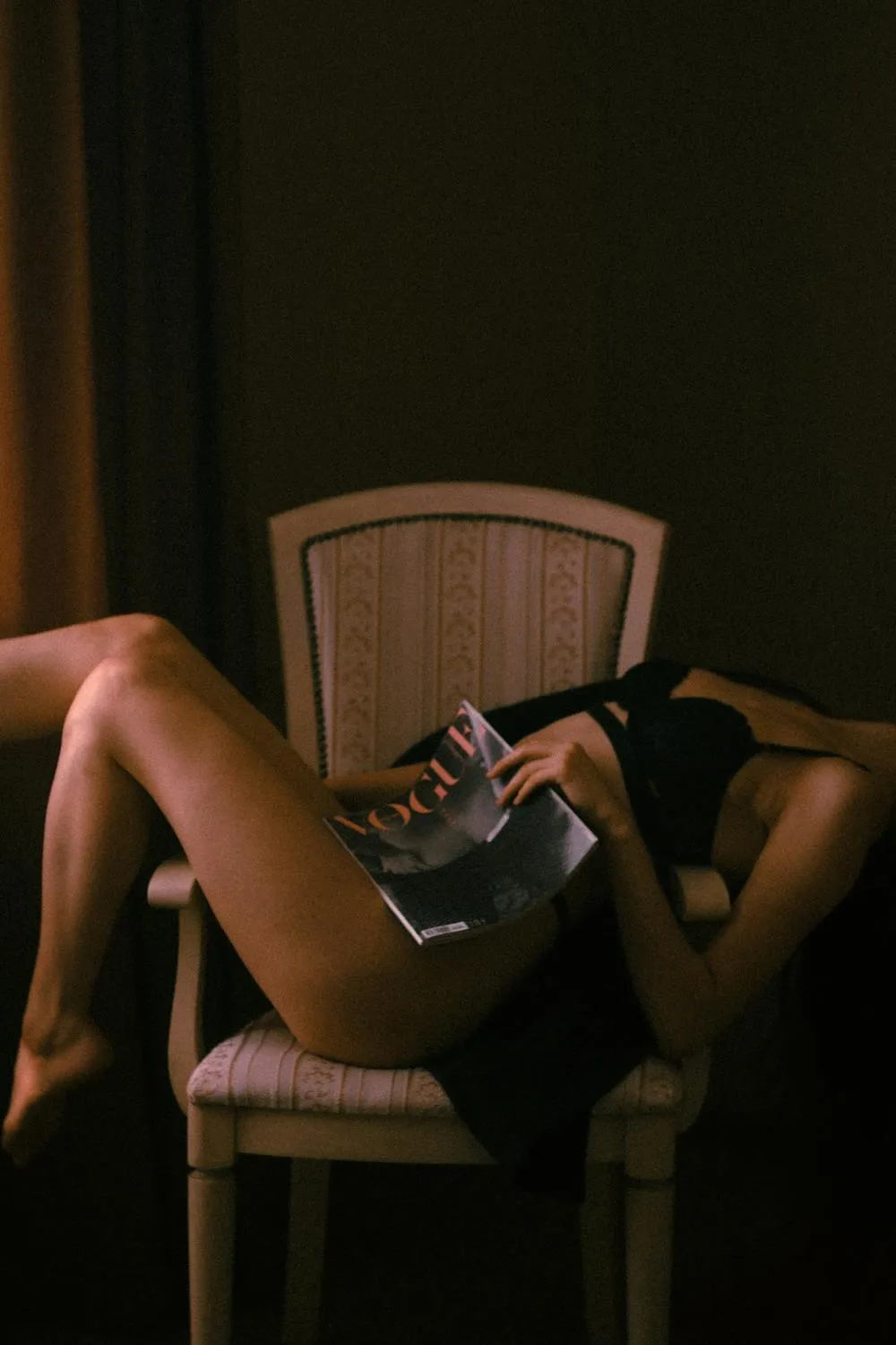 Woman Lounging on a Chair While Reading in Dimly Lit Room