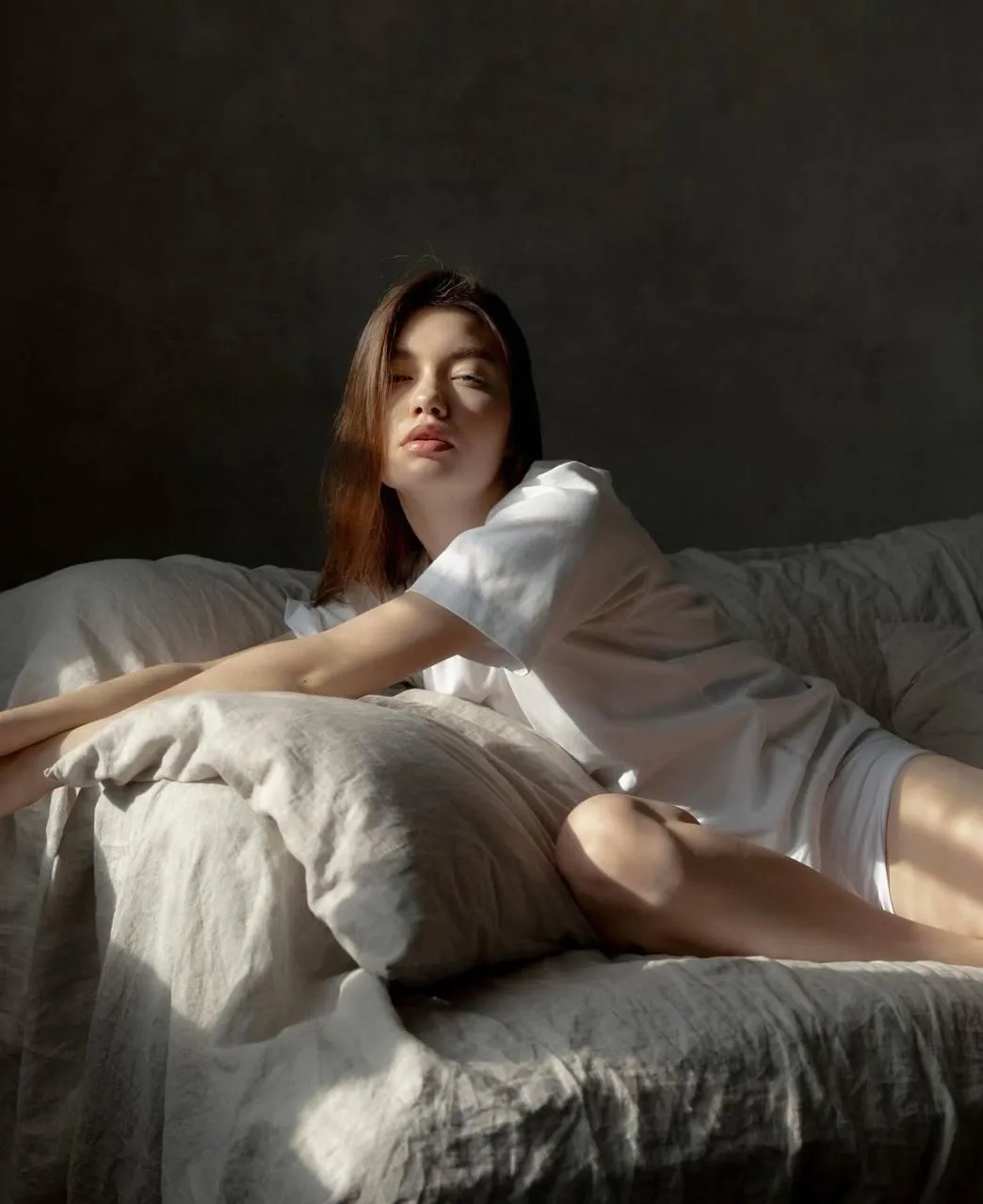 Woman lounging on bed in soft morning light in neutral room