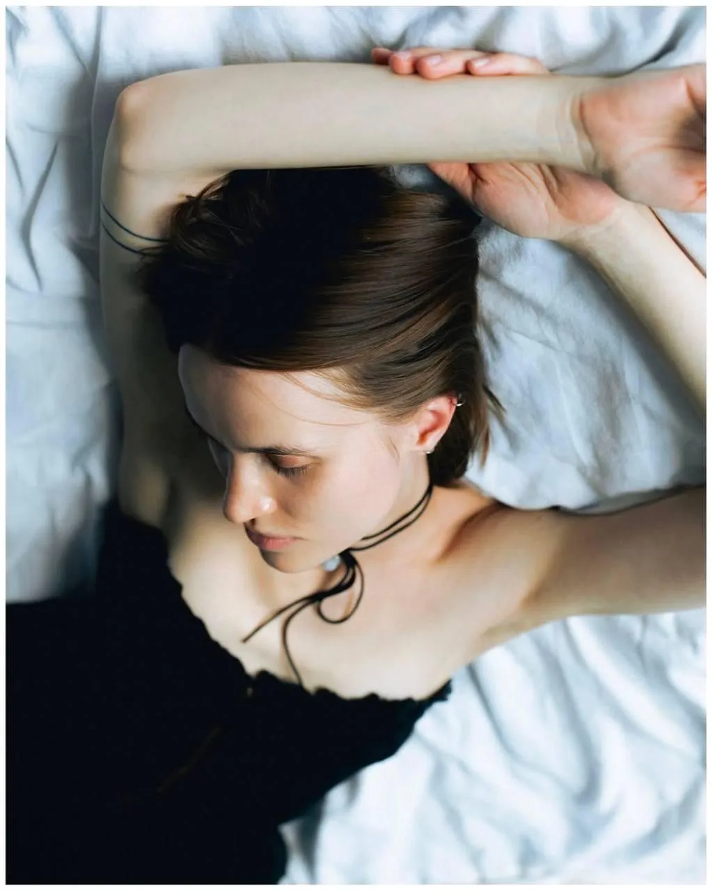 Woman lying on a white bed with soft arms over her face