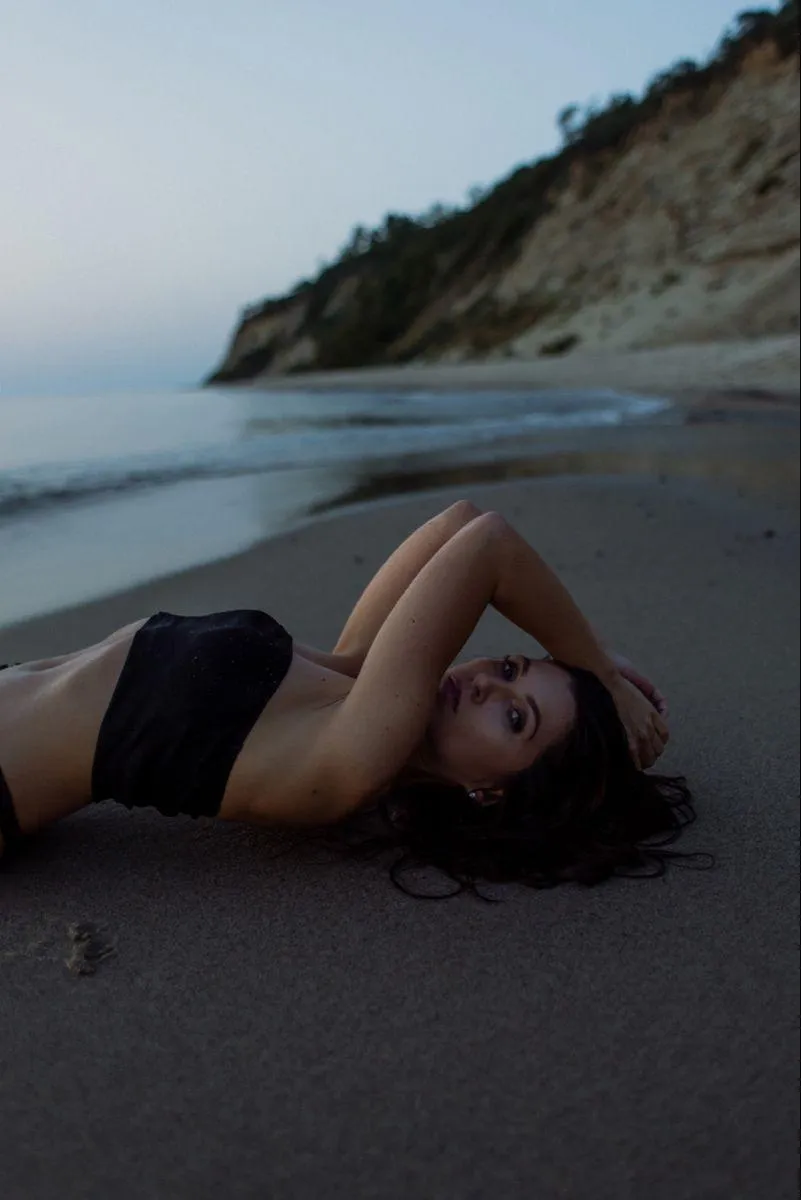 Woman lying on beach sand wearing a stylish black dress