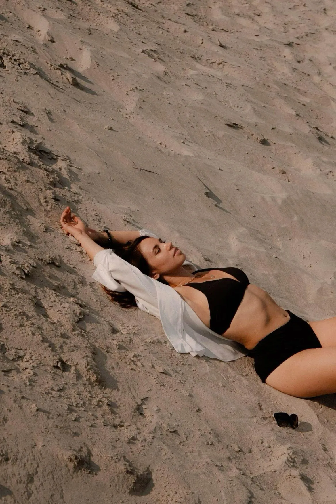 Woman Lying on Sandy Beach Enjoying Sun in a Black Swimsuit