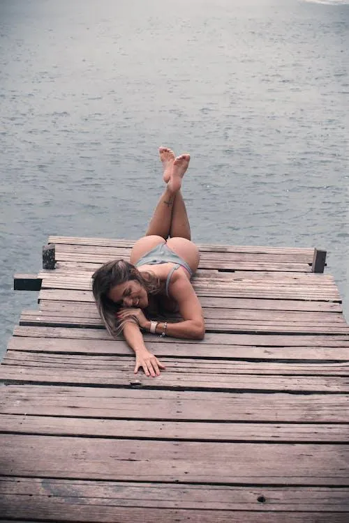 Woman relaxing on a wooden dock by the water in a swimsuit
