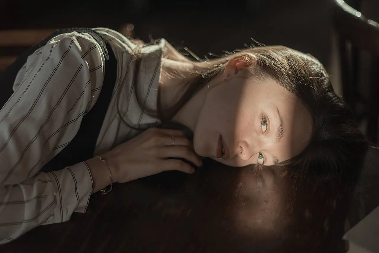 Woman resting her head on a wooden table under warm lighting