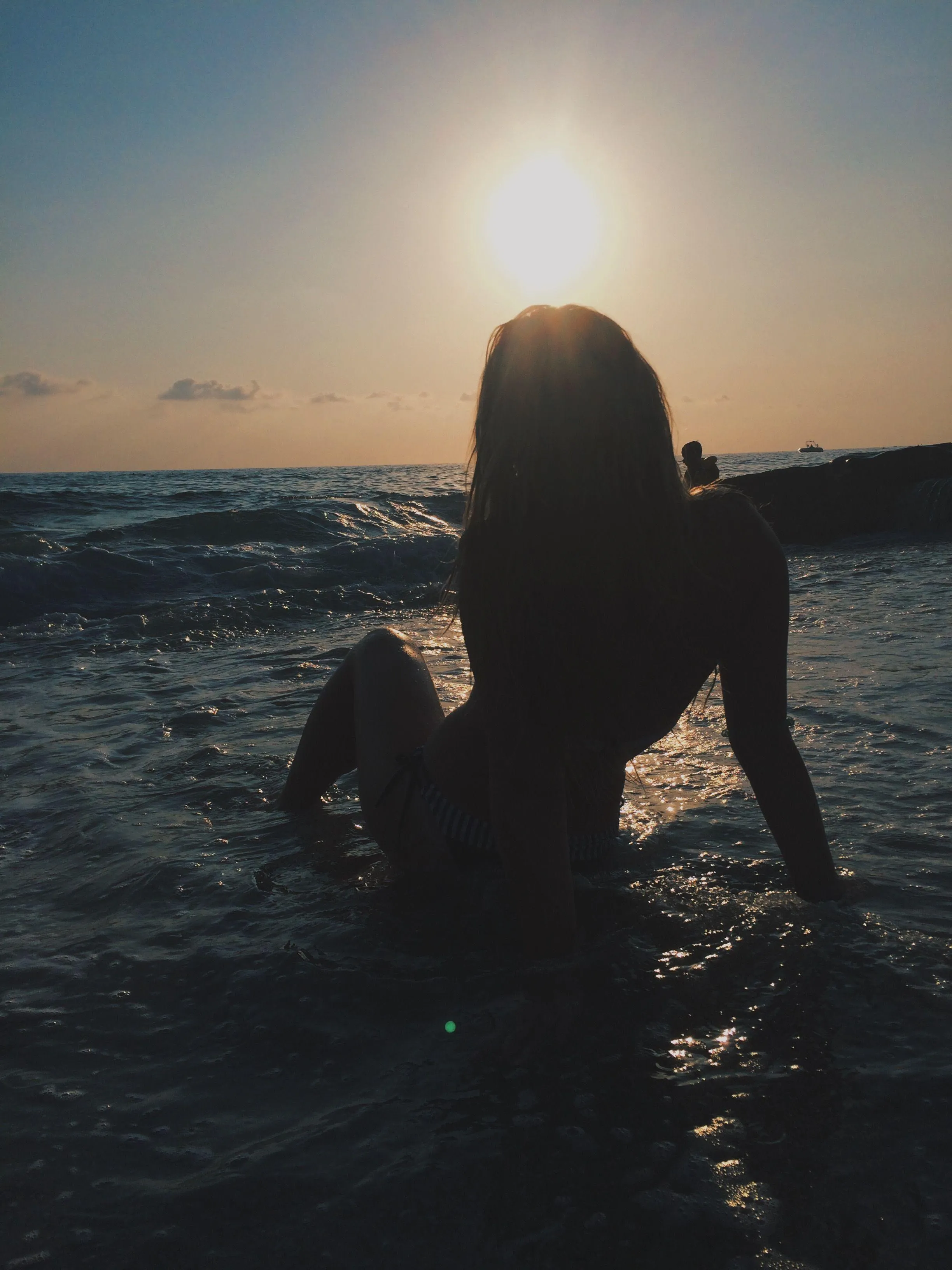 Woman Sitting in the Ocean Waves Watching the Sunset Glow