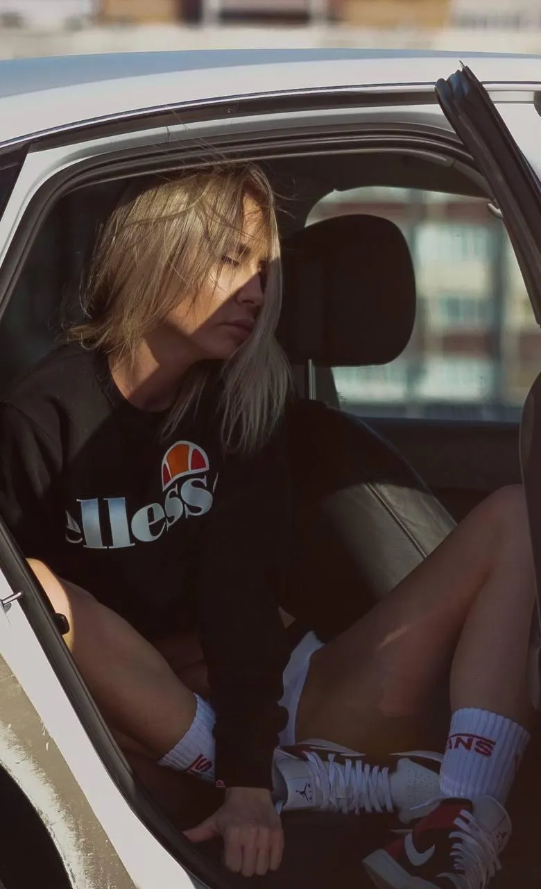 Woman sitting inside a car wearing streetwear and sneakers