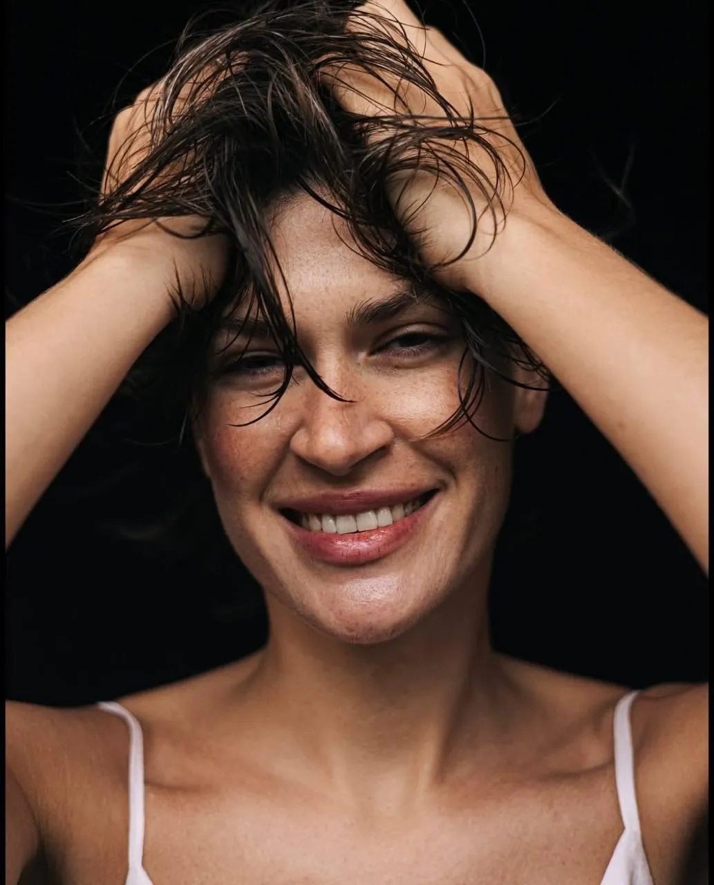 Woman Smiling Happily with Hands in Hair in a White Tank Top
