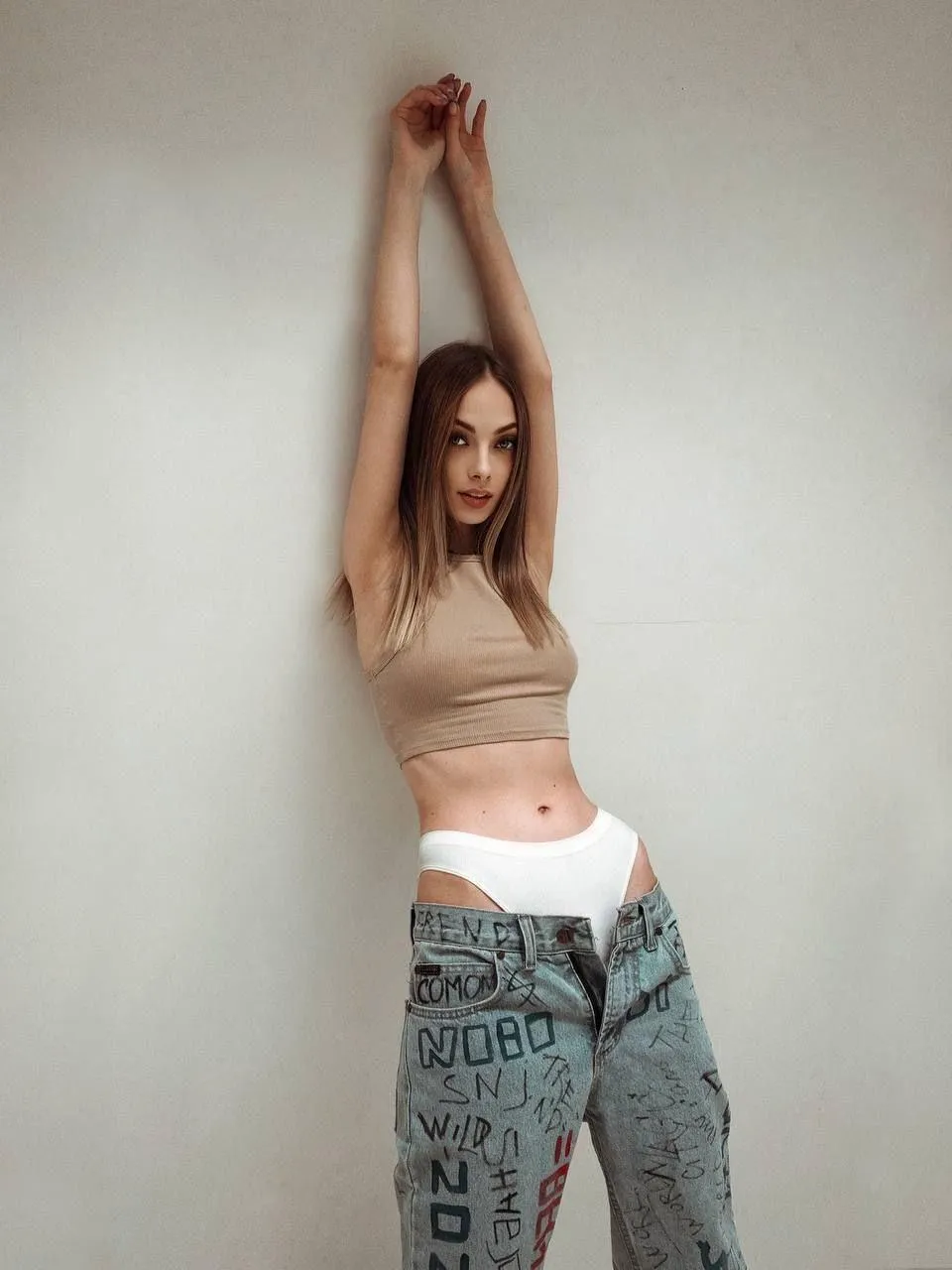 Woman Stretching Up Wearing Casual Clothes Near Plain Wall