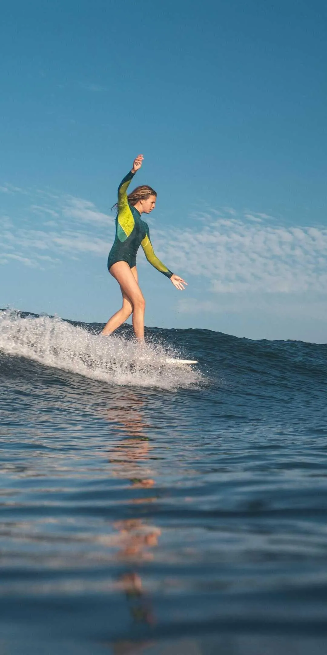 Woman Surfing on Ocean Wave Wearing a Wetsuit Under Blue Sky