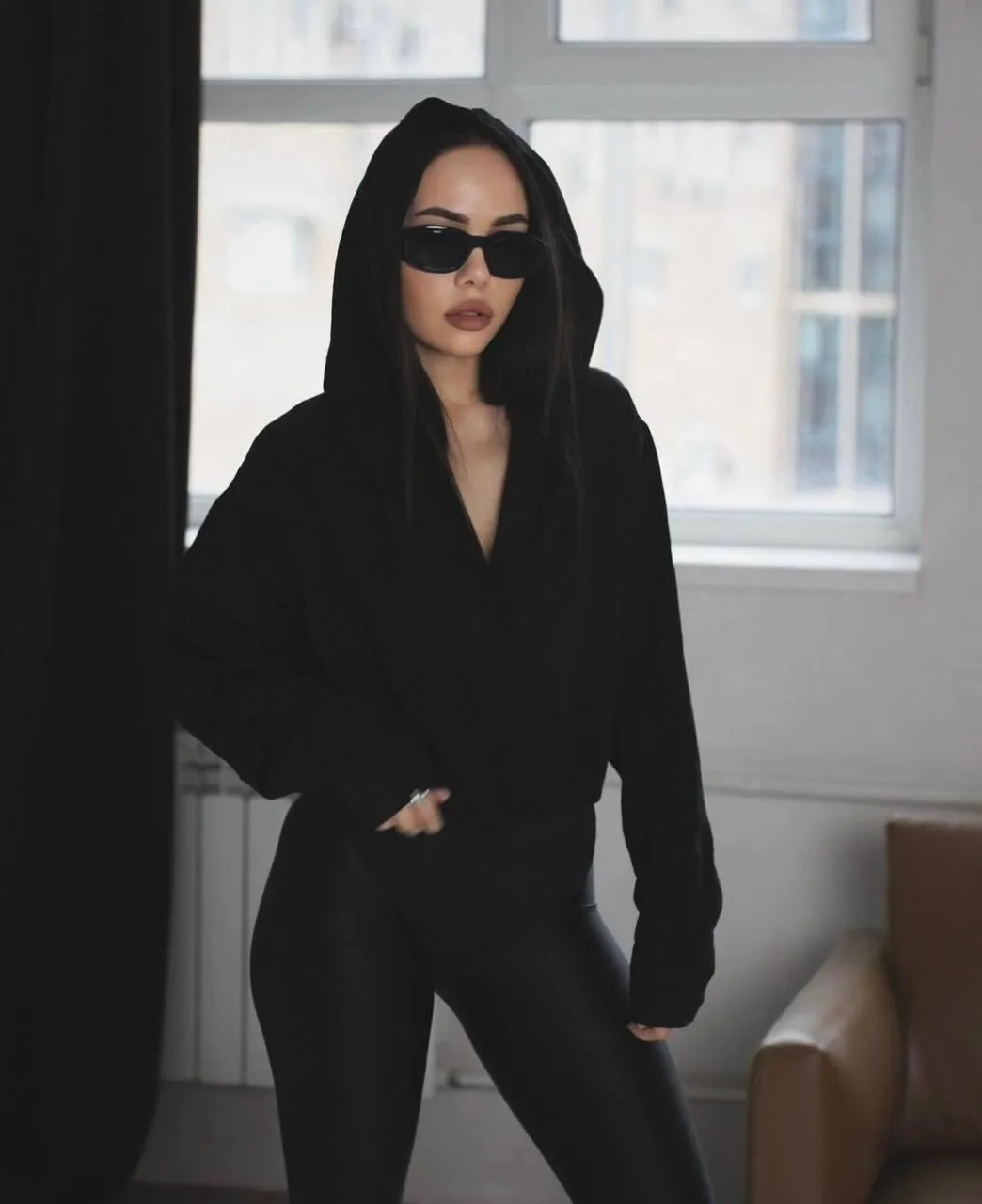 Woman wearing a black hoodie with sunglasses near the sofa