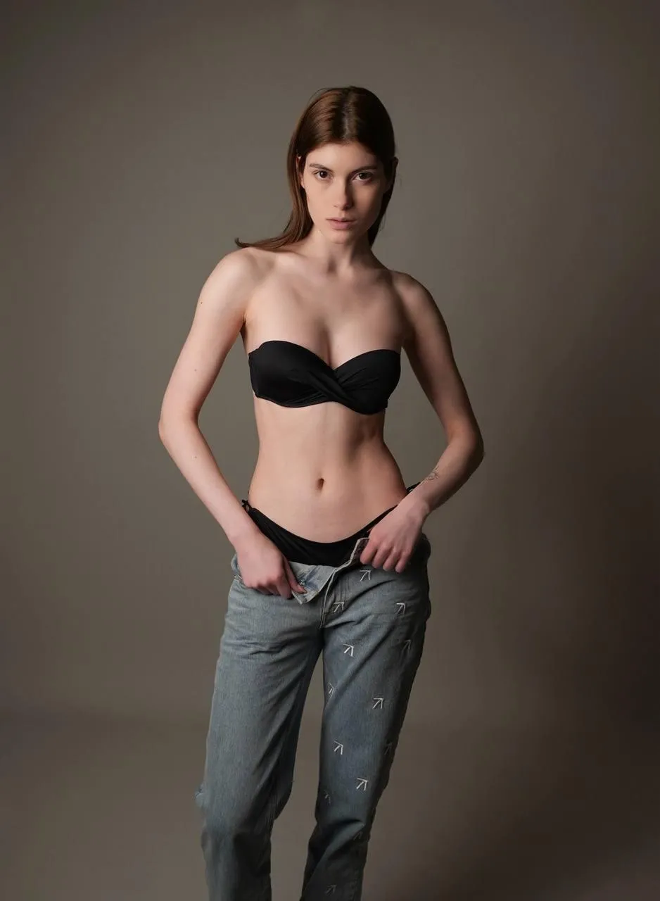 woman with a black top and gray jeans standing in the studio