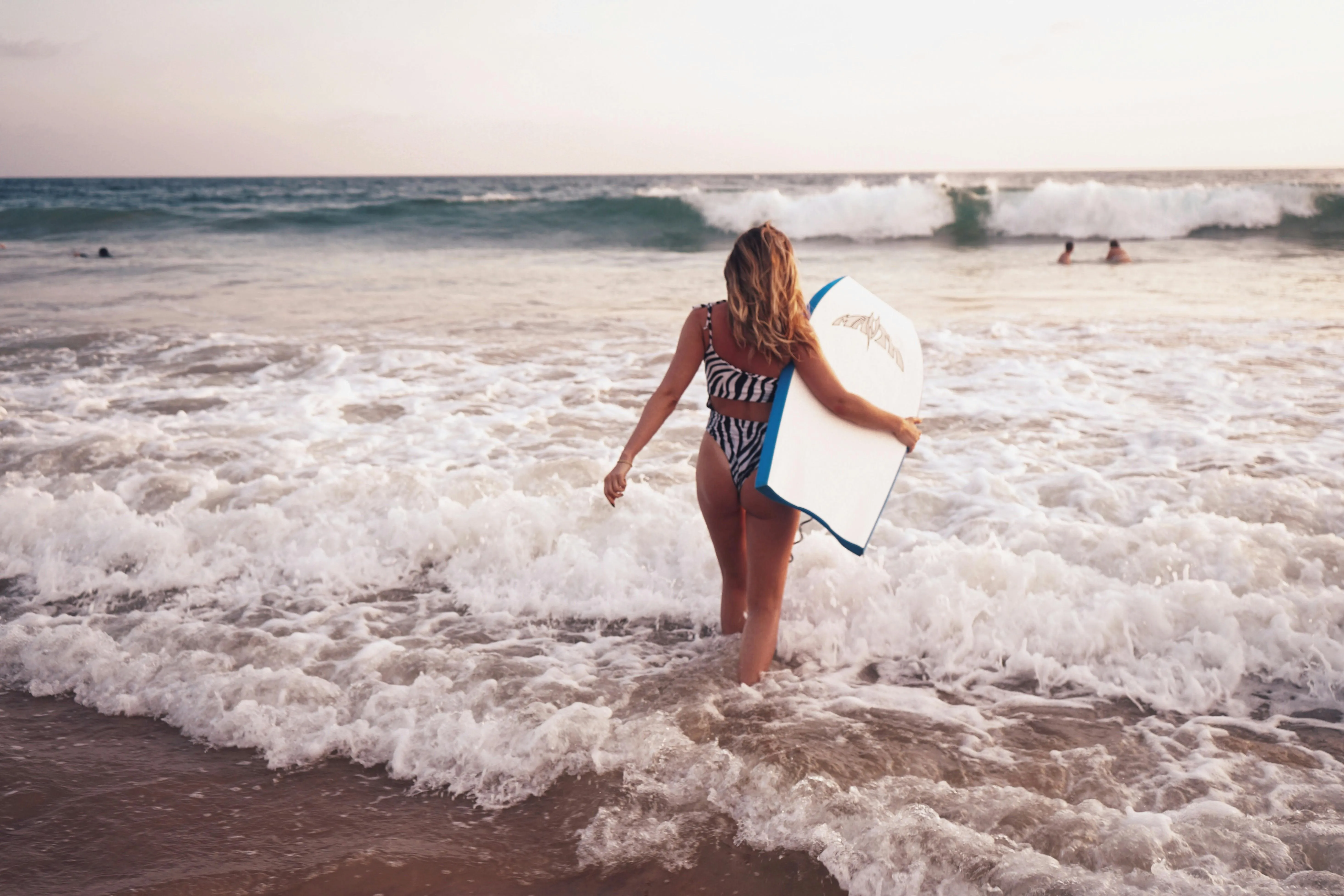 Woman with a Surfboard Walking on a Shallow Beach Surf