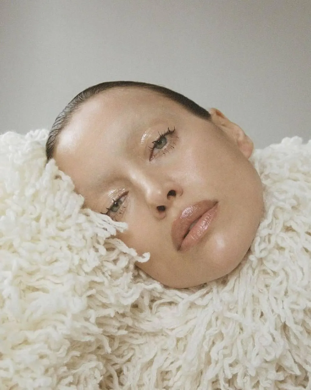 Woman with Shaved Head Resting on Furry White Blanket Image
