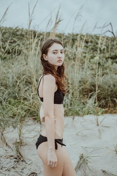 Young girl standing on the beach sand wearing a black bikini