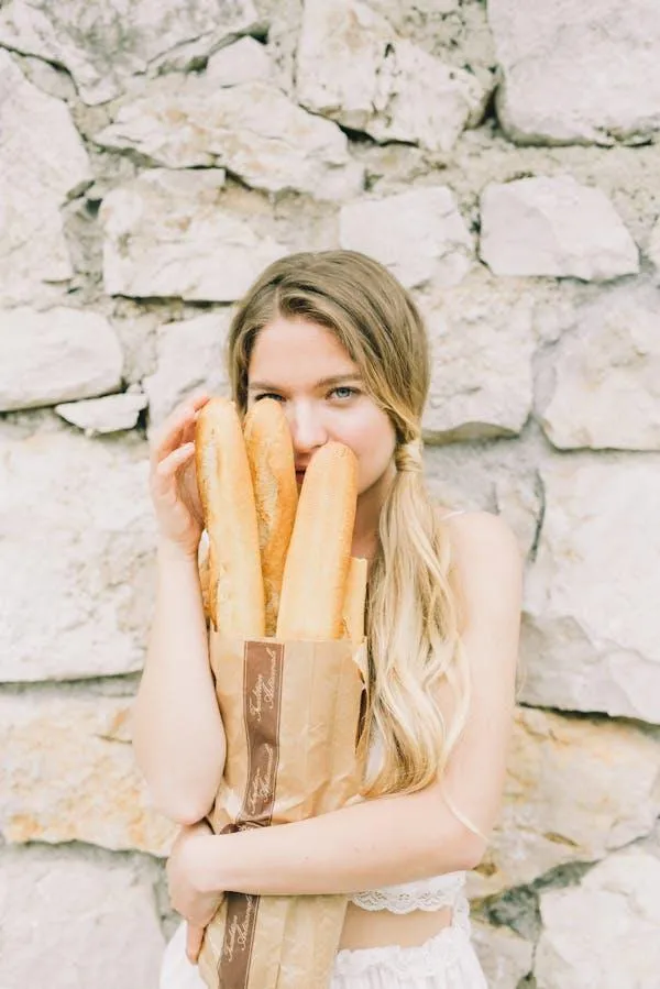 Young woman holding baguettes in front of a stone wall photo