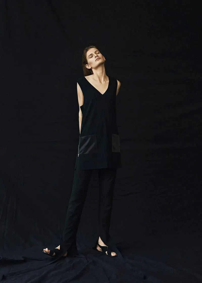 Young woman in a black outfit standing near black backdrop