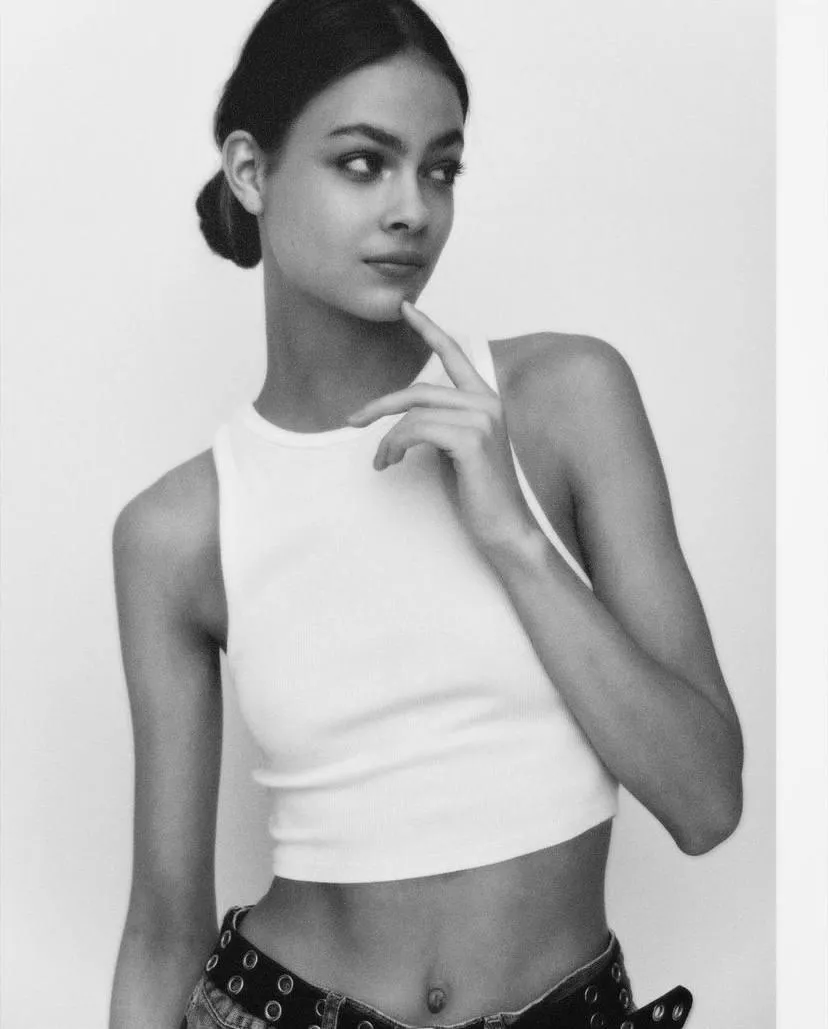 Young woman in a white top posing against a plain background