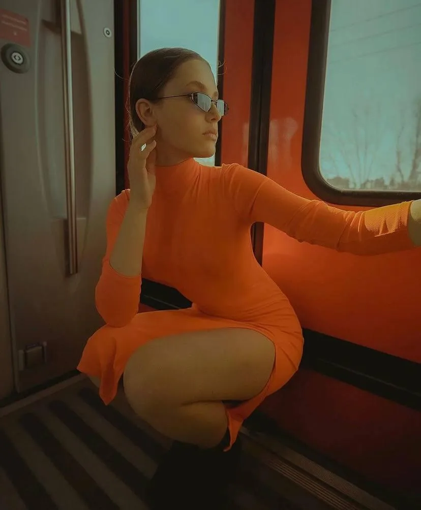 Young woman squatting near the train door with orange dress