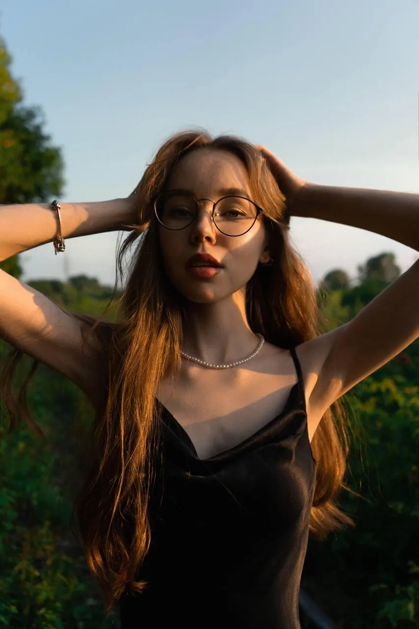 Young woman with glasses and long hair posing in sunlight