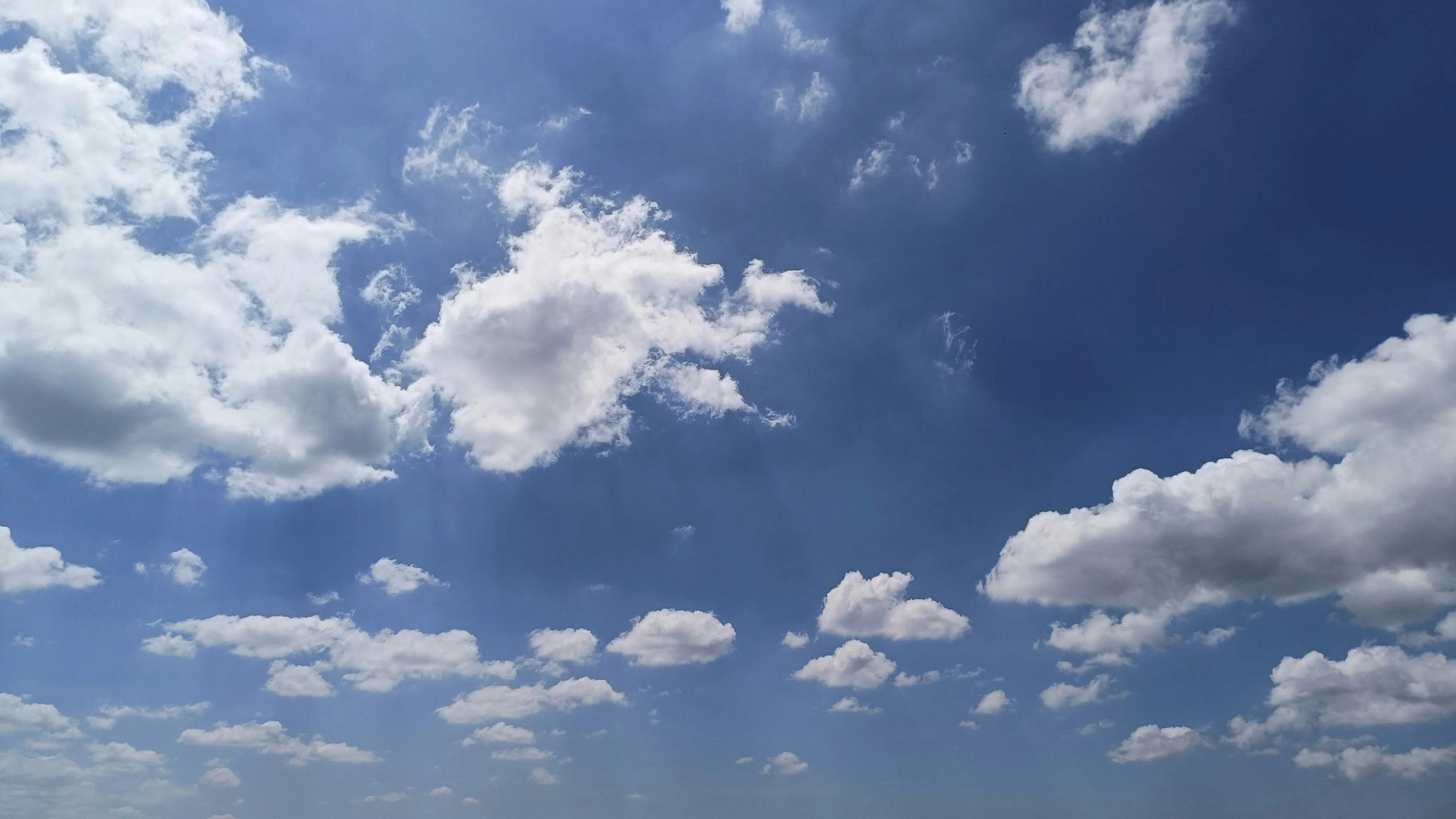 Bright Blue Sky with White Fluffy Clouds Over Horizon