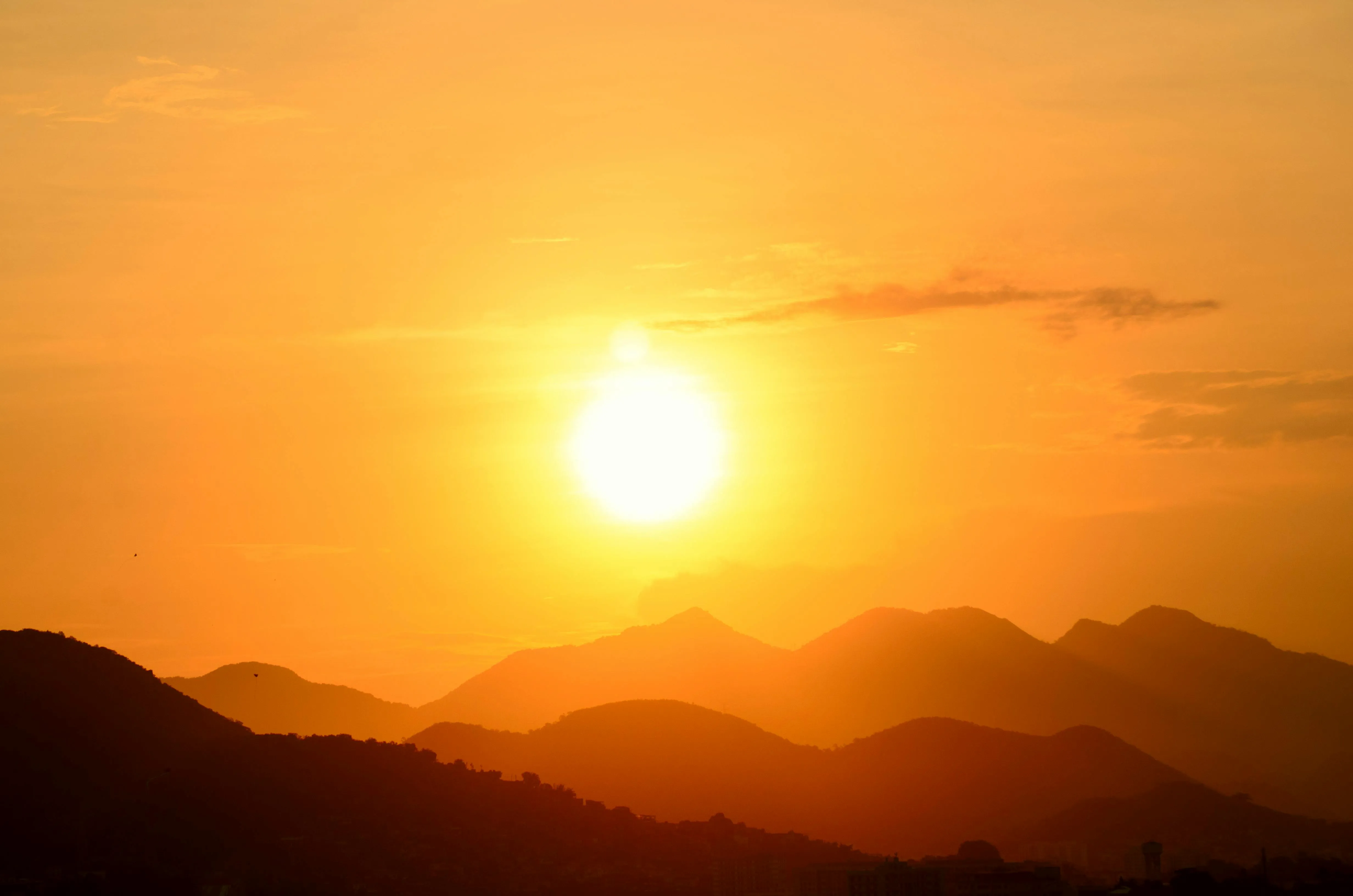 Bright Sun Setting Behind Distant Hills and Clouds Image