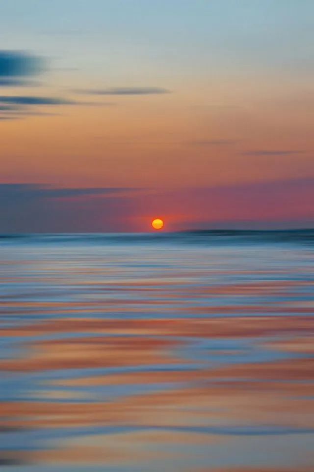 Calm Ocean Sunset with Soft Clouds Reflecting in Water