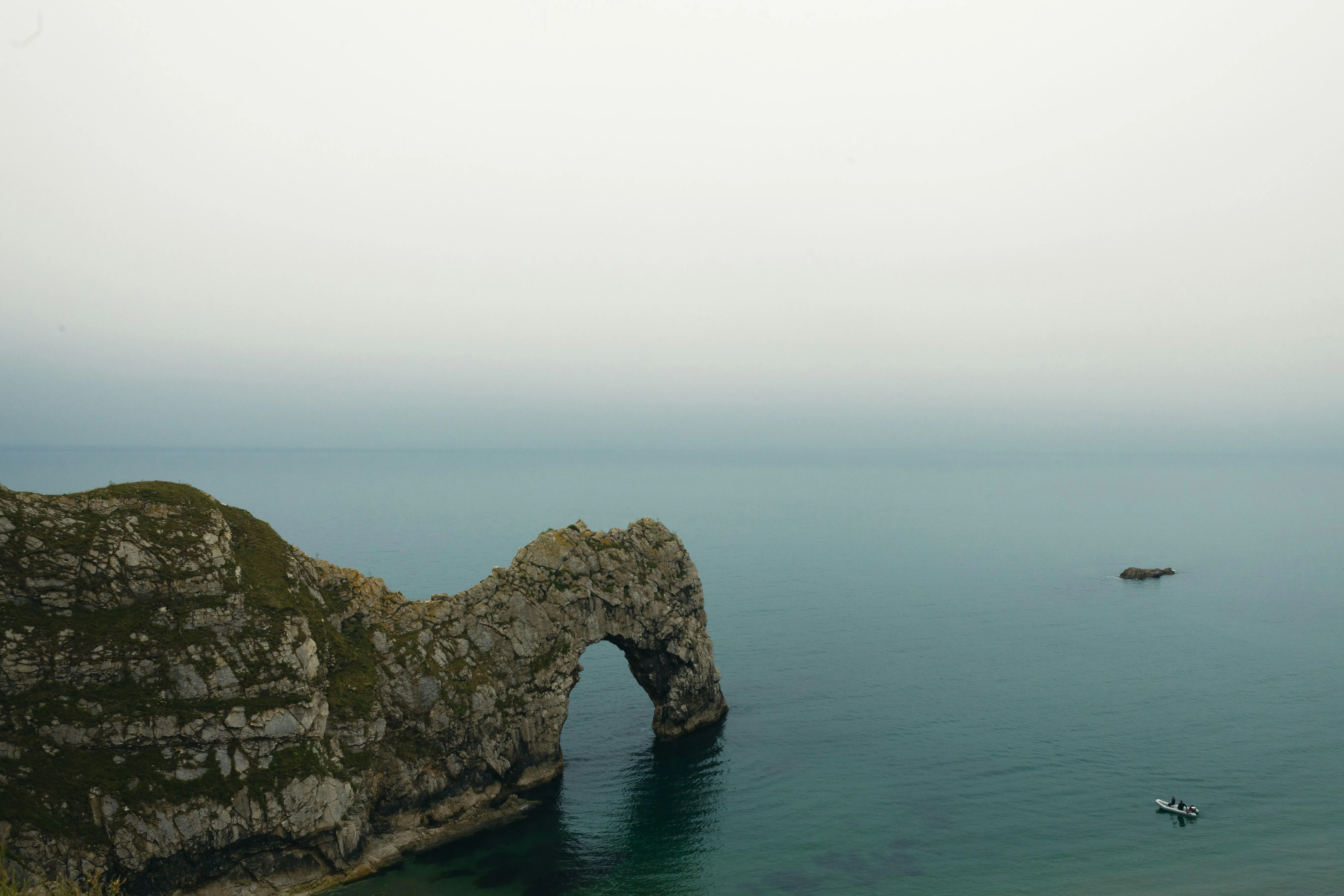 Calm sea horizon viewed from rocky cliff under foggy sky