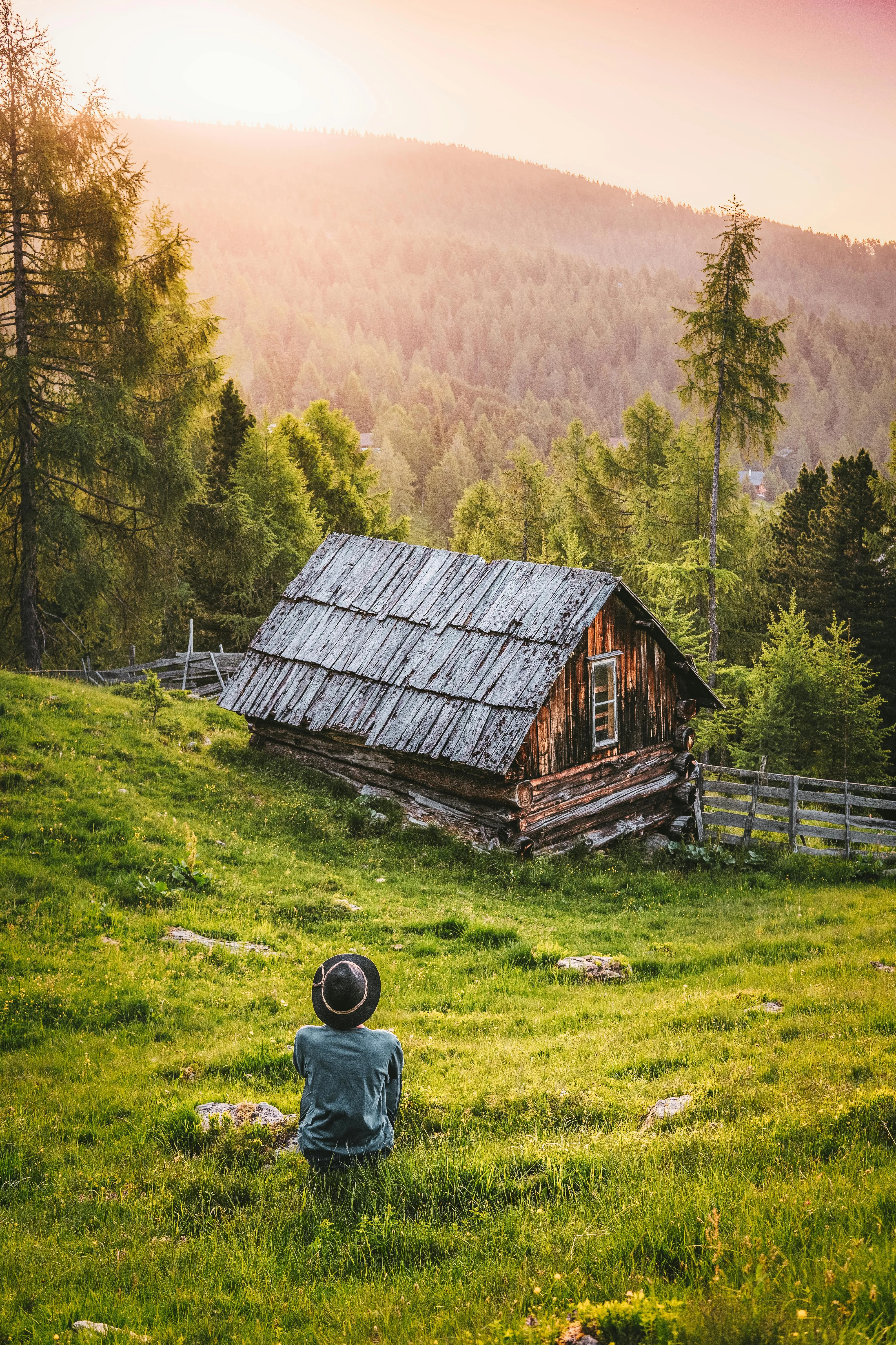 Child Sitting Near Cabin Under Warm Sunset and Clouds