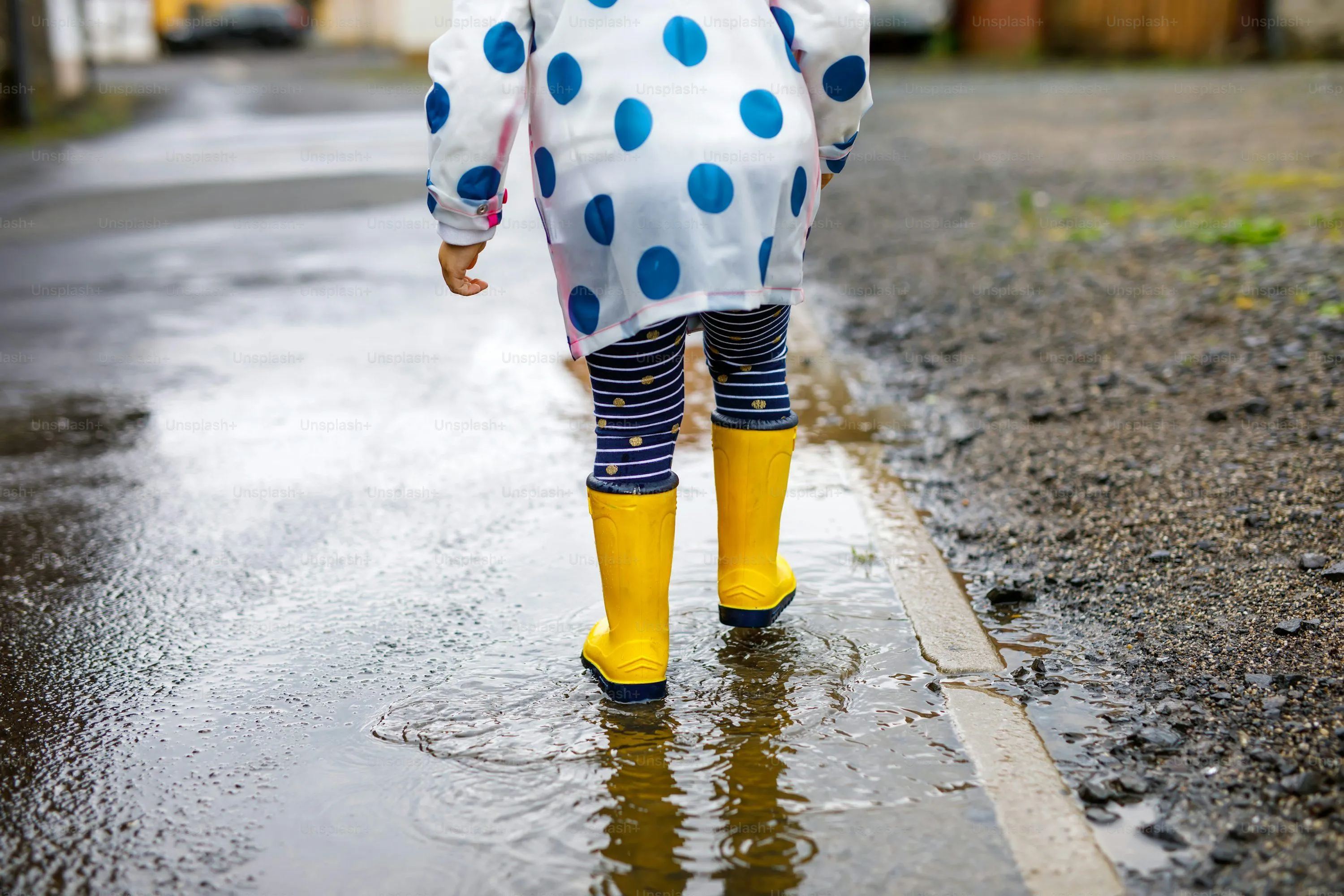 Child Wearing Yellow Boots Walking on Wet Pavement