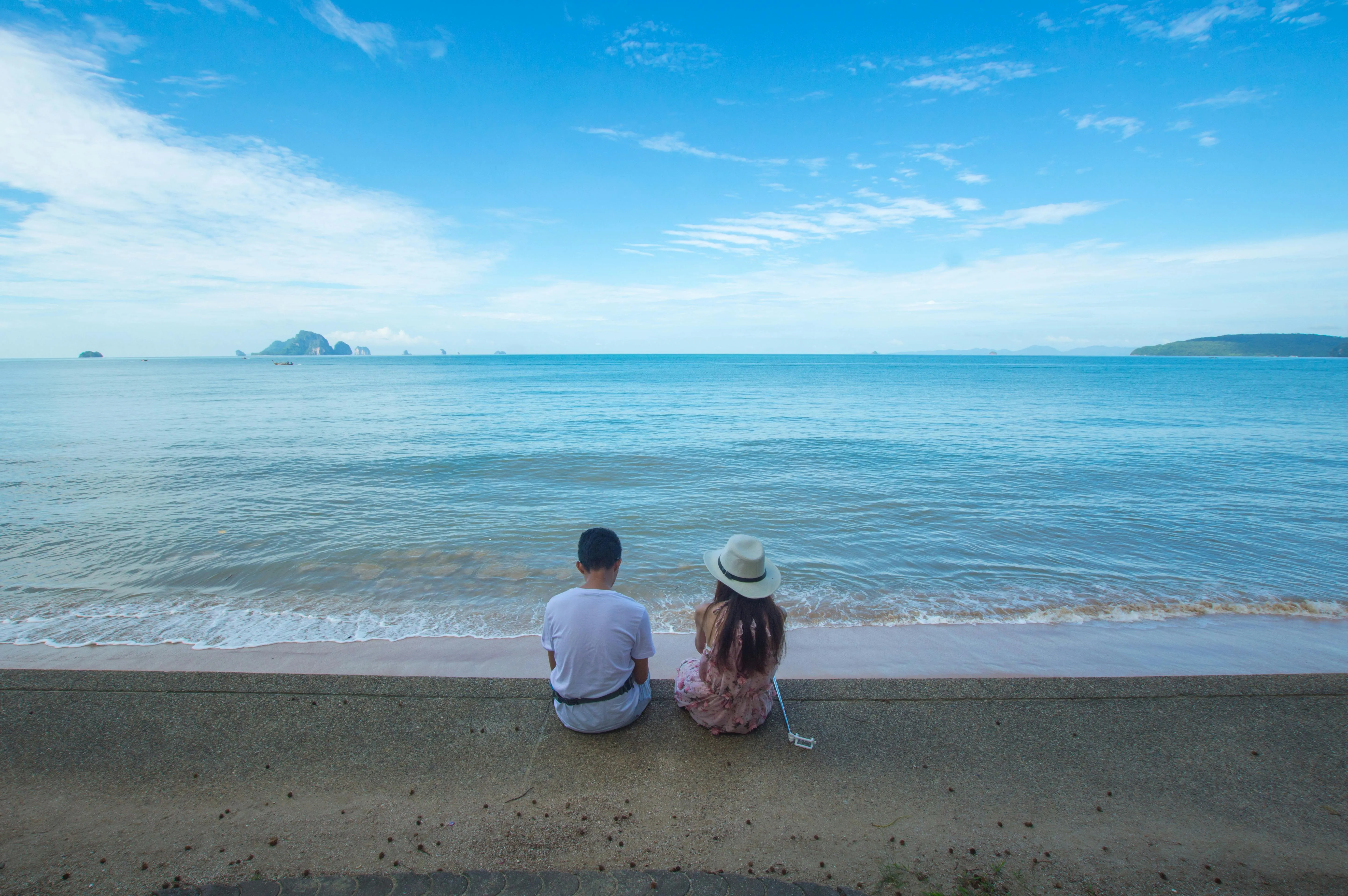 Couple Sitting at the Beach Under a Blue Sky Wallpaper