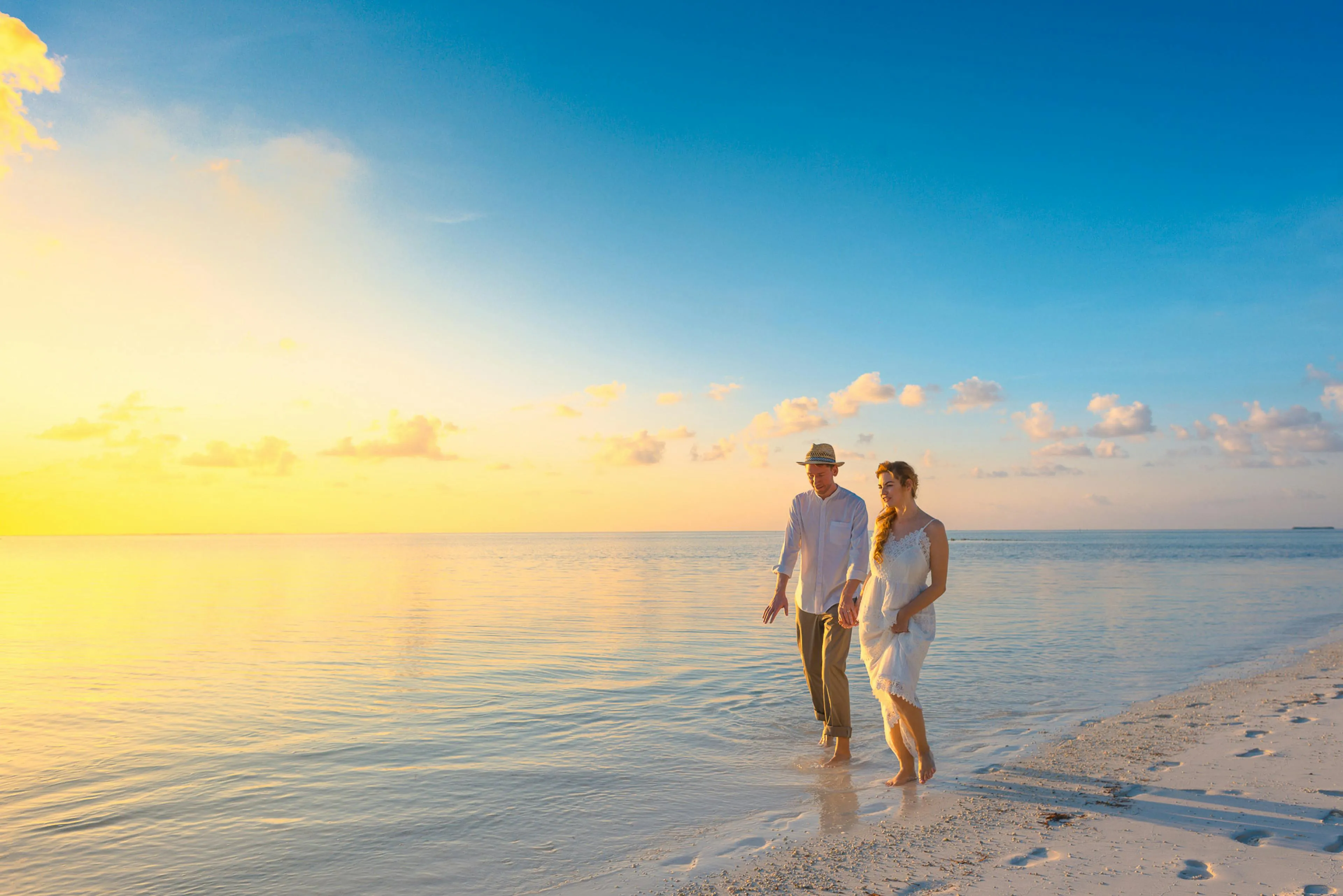Couple Walking on Beach at Sunset Under Calm Sky Wallpaper