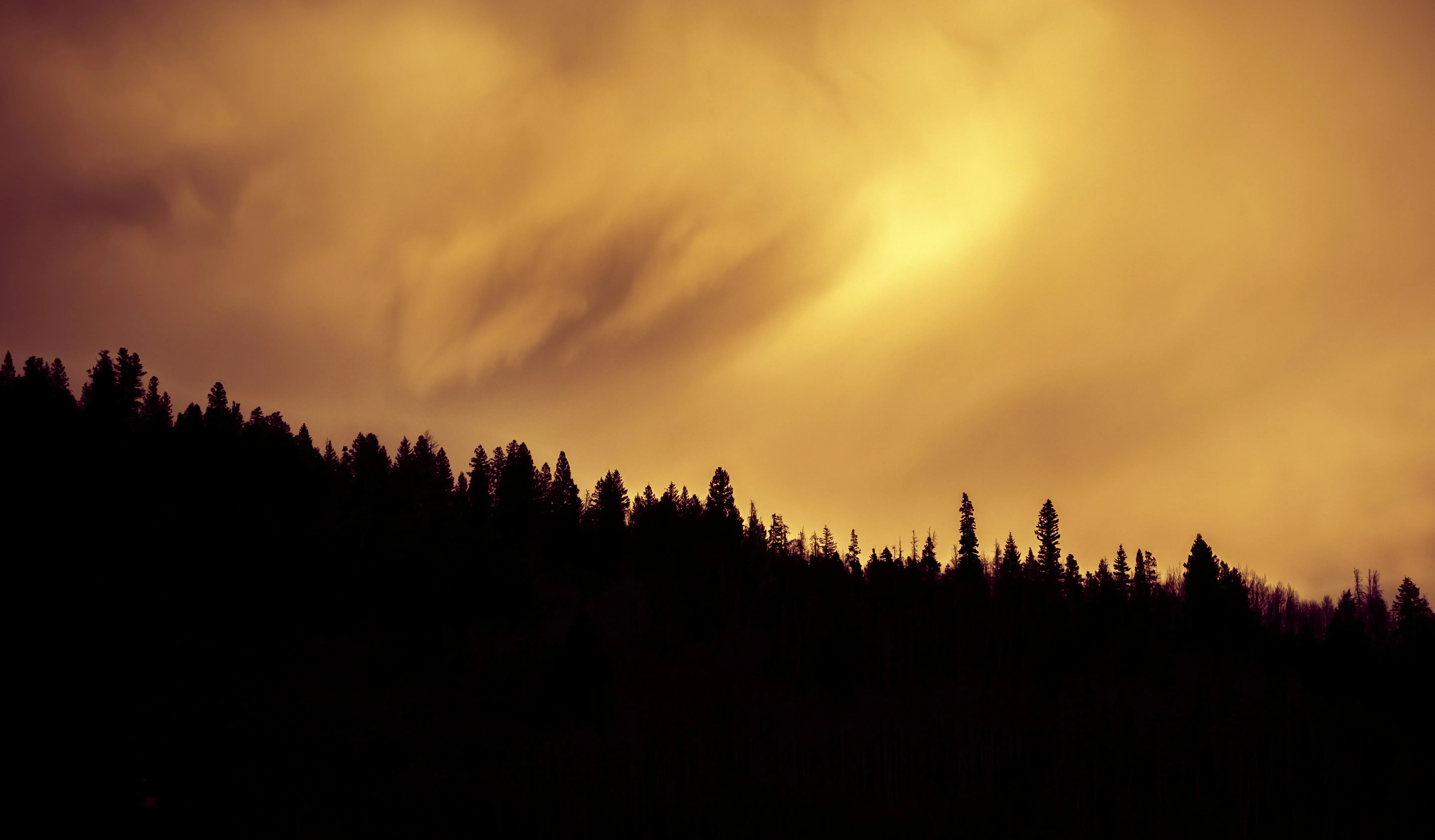 Dark Orange Clouds Swirling During Sunset Over Tree Line