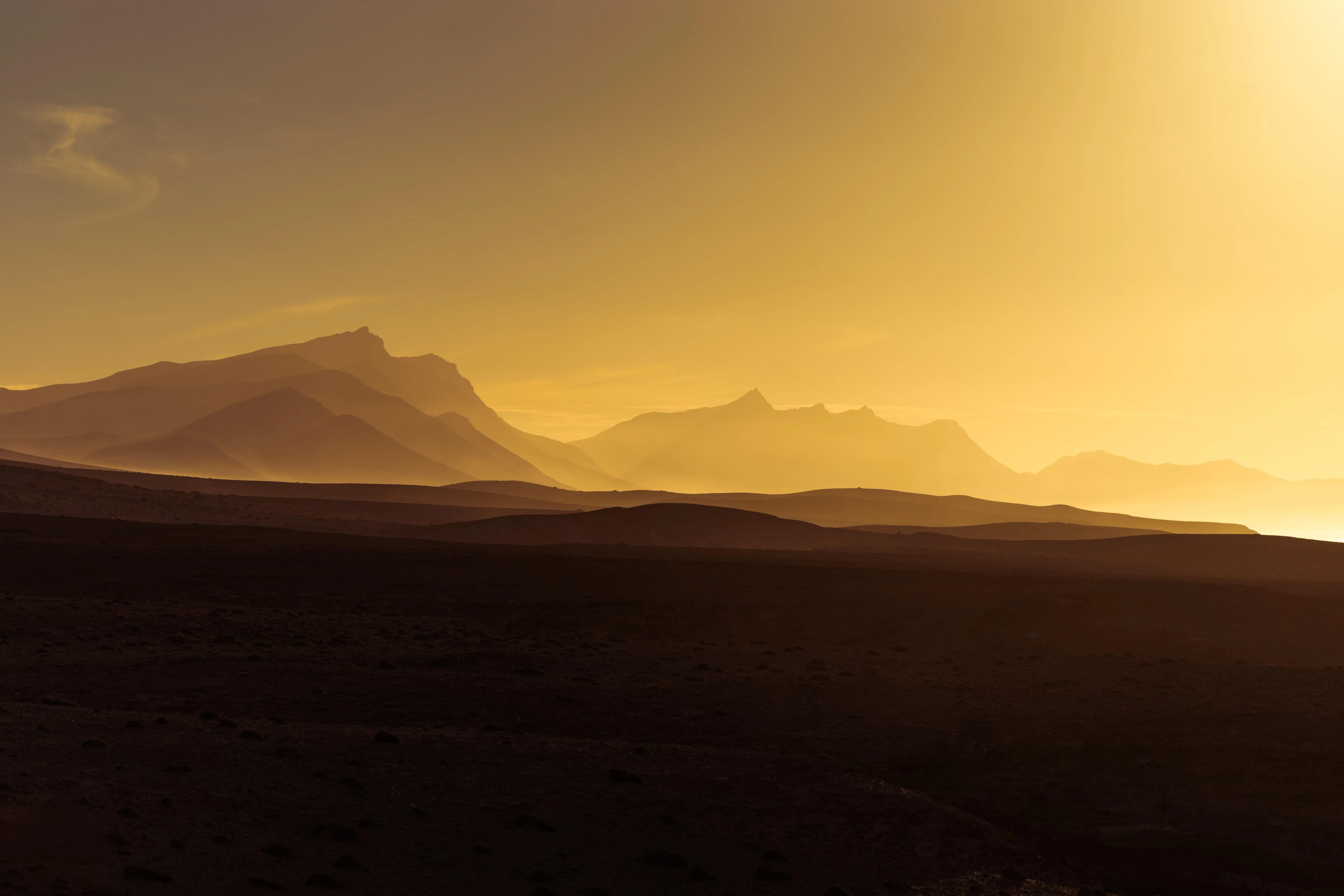 Distant desert dunes under soft orange setting sun