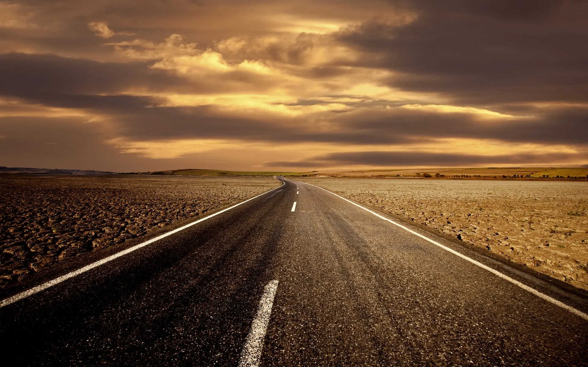 Empty Road Leading Toward Golden Sunset Over Vast Landscape